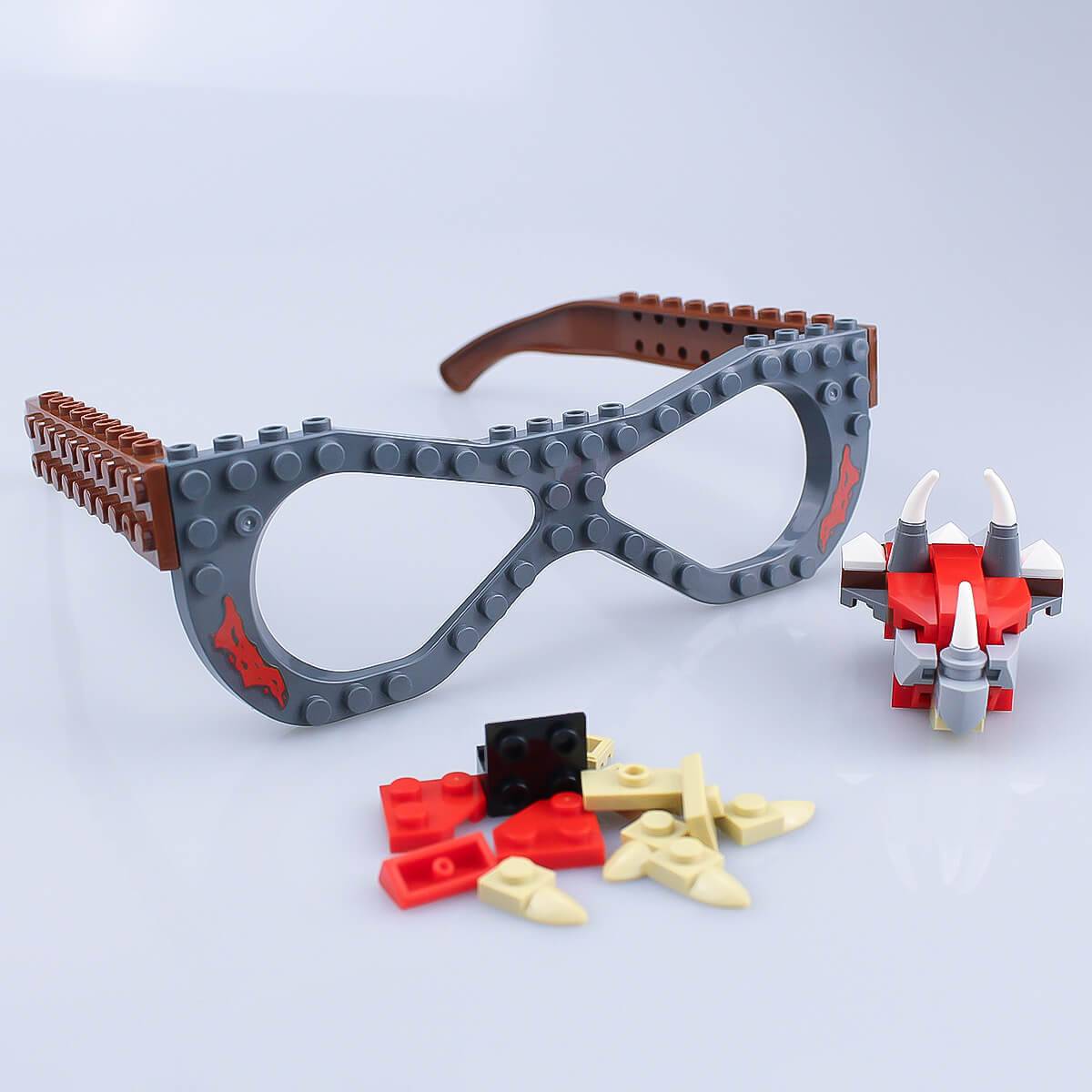 Unassembled dinosaur-themed Kids DIY Glasses Building Block Set with gray and brown frames and various building pieces. Encourages hands-on creativity.