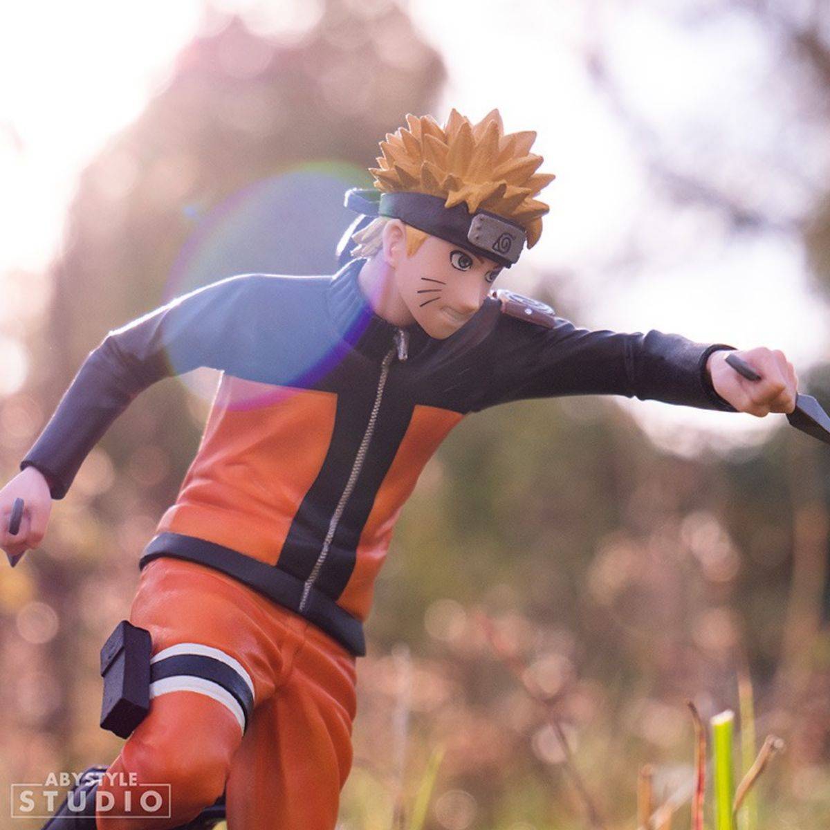 Outdoor scene of ABYstyle Studio Naruto Shippuden Naruto SFC Figure 17cm in mid-action, wielding kunais with a determined expression.