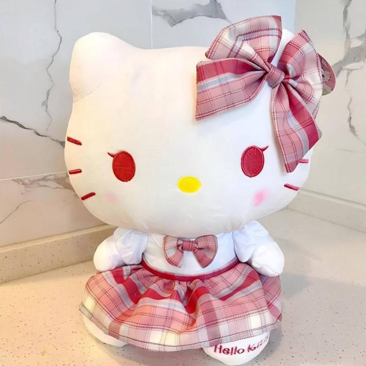 Sanrio JK Series Hello Kitty plush toy 28cm displayed on a countertop, featuring a pink plaid schoolgirl outfit. A soft and adorable collectible plush.