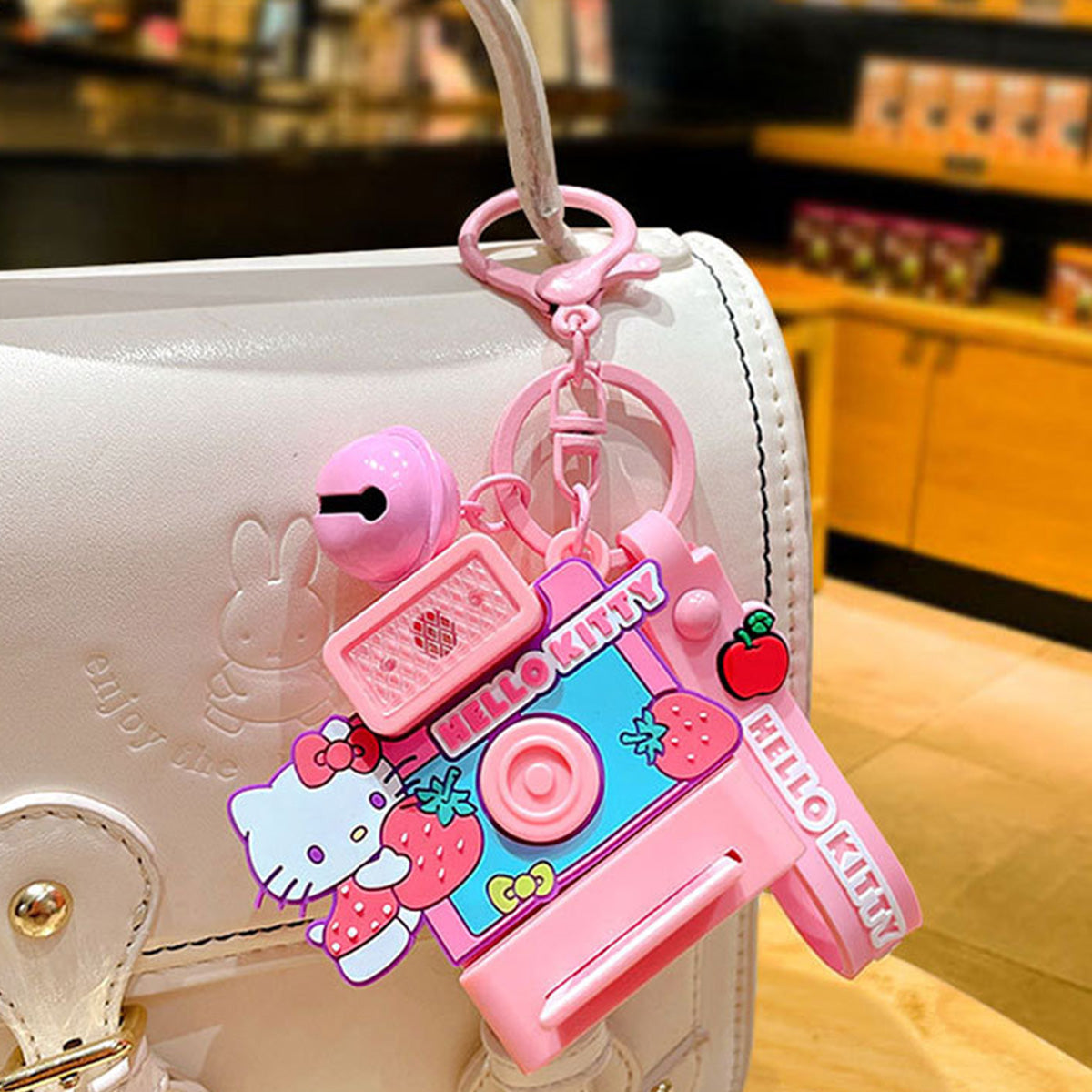 Hello Kitty Sanrio Characters Polaroid Camera Keychain attached to a white handbag, showcasing its stylish and cute design as a fashionable accessory.