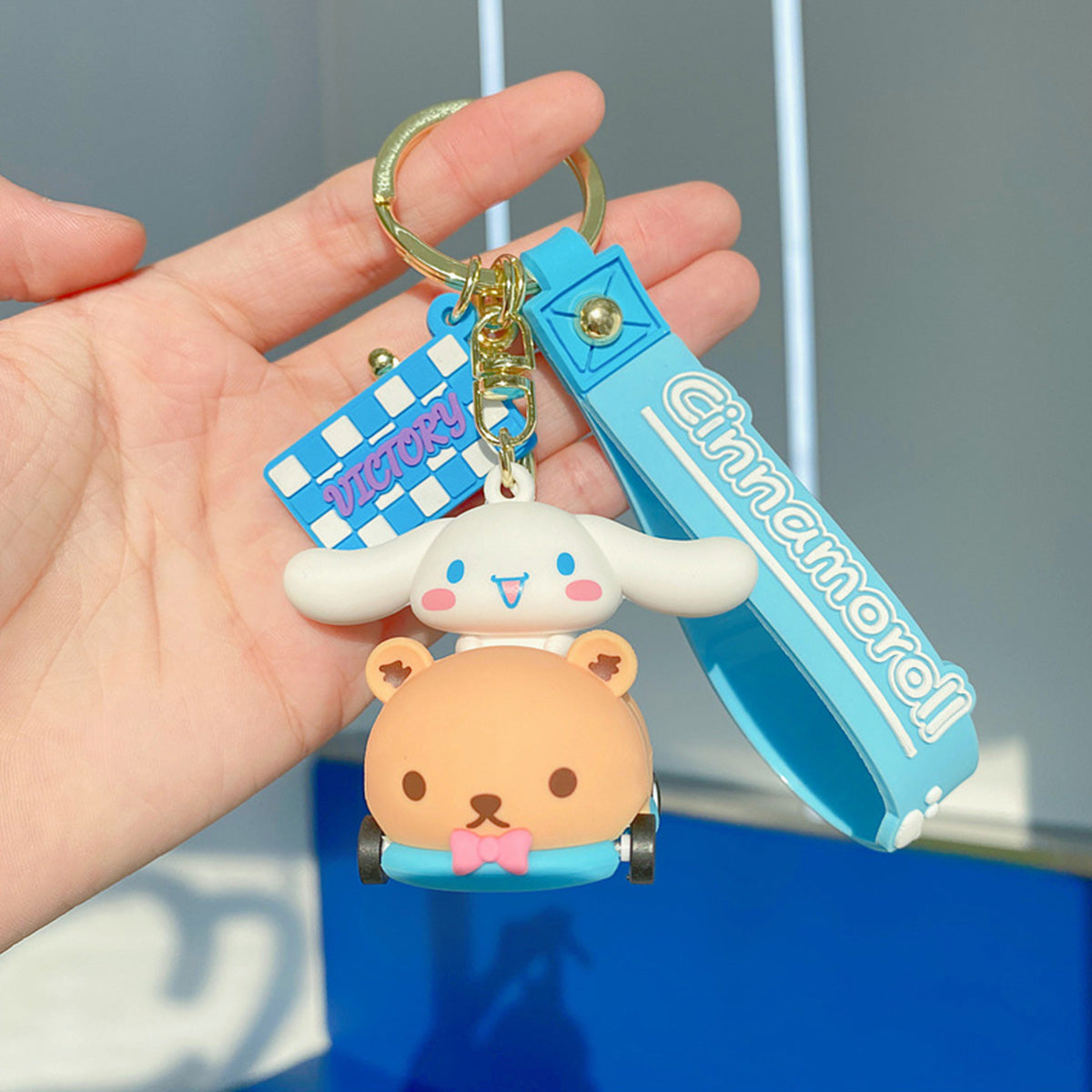 Sanrio on Race Car with Rolling Wheel Keychain featuring Cinnamoroll in a bear-themed car with a blue wrist strap and 'VICTORY' charm.